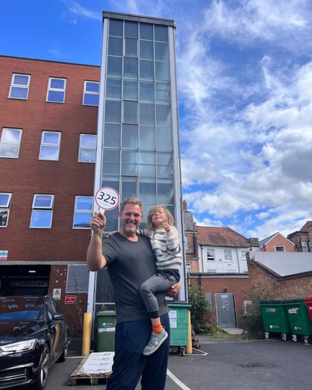 Squibb smiles as he holds his son Aidan and an auction paddle in his other hand with the glass stairwell and attached building behind