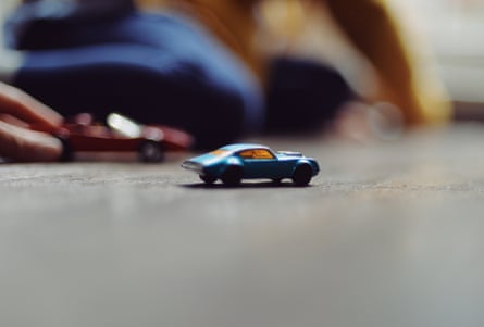 A blue toy car on a floor with blurred figures of children in the background