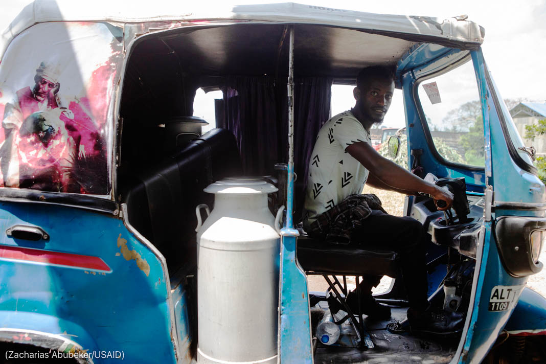 Man at wheel of vehicle carrying large container of milk (Zacharias Abubeker/USAID)