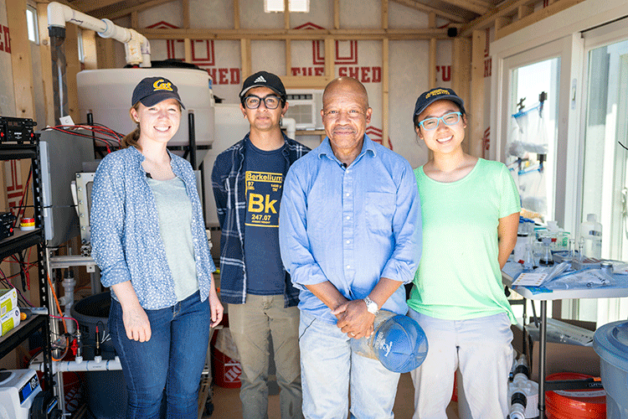 Four people stand together for a group photo with the arsenic treatment system at a farm.