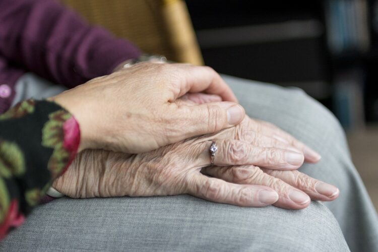 An older person's hand is held by a younger person's hand.