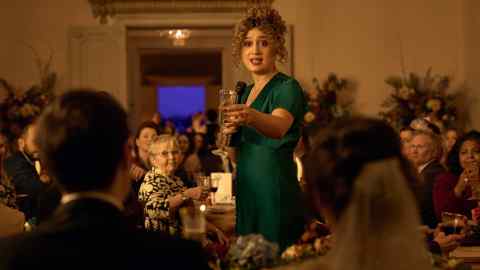 A woman in a green dress stands making a toast at a wedding reception