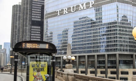 A windowed high-rise building with the word in white 'Trump' halfway up, looming over a bend in a river we assume is below a concrete walkway.