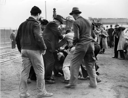 men in hats viewed from behind next to what appears to be a pile of people grappling with each other