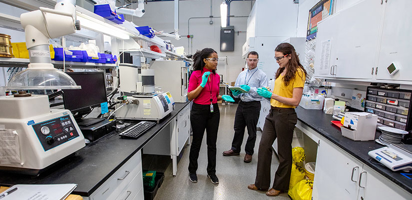 Three researchers standing and talking in a laboratory.