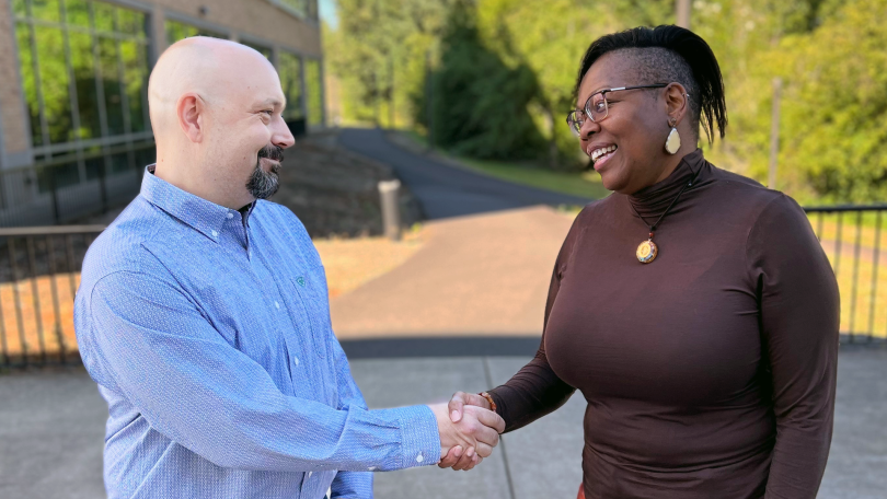 Brian and Rakiah shake hands, smiling, outside Fisher Investments’ office. 