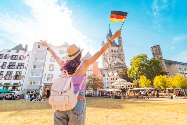 A young happy tourist or student girl with a German flag at the old town or Altstadt in Cologne fish market square. Studying language abroad and traveling concept