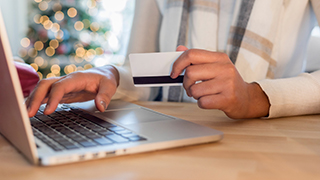 Woman holding a credit card in one hand while typing on her laptop with the other.