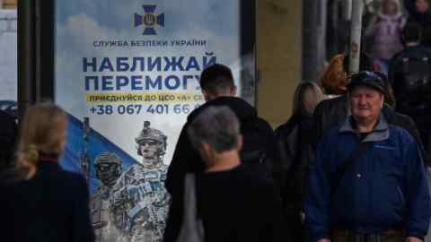 People walk past a poster depicting Ukrainian servicemen and a slogan which reads “Bring the victory soon” in Kyiv