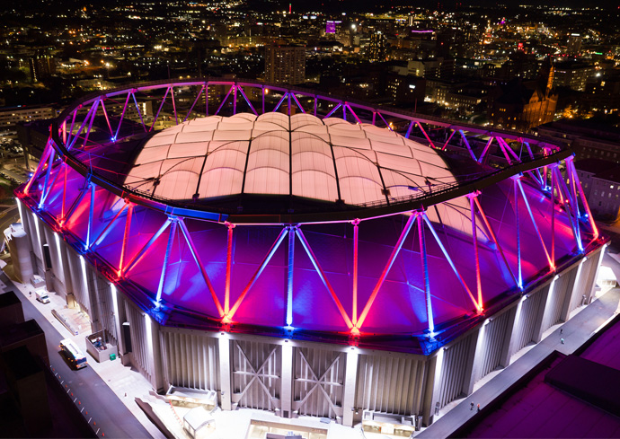 aerial photo of JMA Wireless Dome on the Syracuse University campus lit up in blue and orange at night