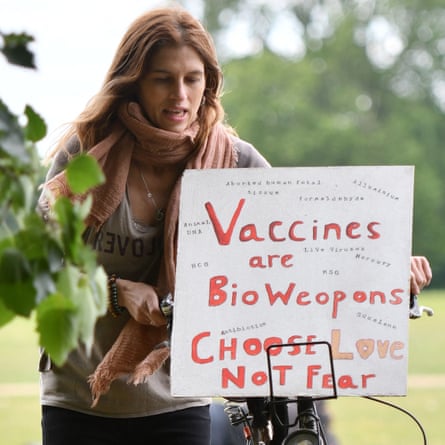 Woman with a scarf and long hair pushing a bike with a sign on it reading: “Vaccines are Bio Weapons. Choose Love not Fear”