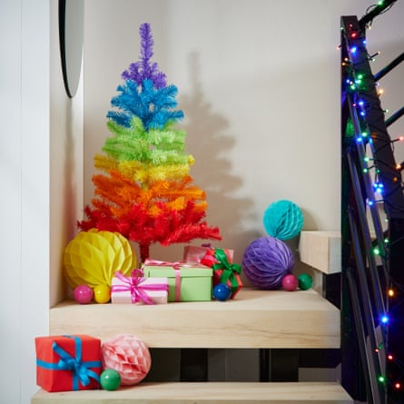 An Argos rainbow Christmas tree on a staircase with fairy lights on the bannister and gifts and baubles nearby