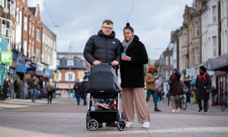 Rachel and Domantas stand smiling for a photograph with a pram in the middle of a pedestrianised shopping street.