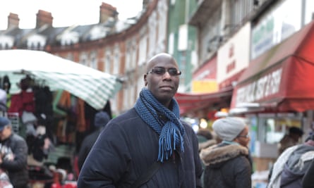 Rasheed Ogunlaru in a coat and scarf in front of a busy street market scene