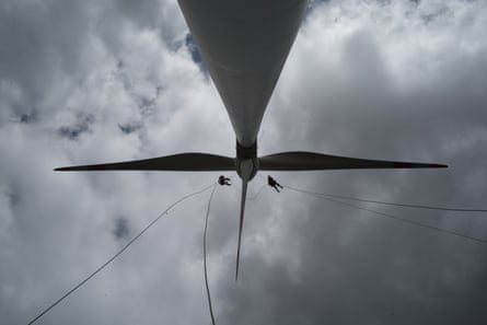 Two workers in harnesses on ropes inspect a wind turbine.