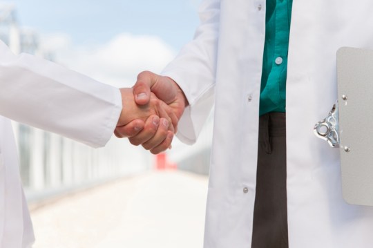 Scientists shaking hands outside greenhouses