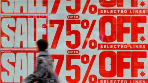 A shopper walks past signs for a sale in a shop window in London, England