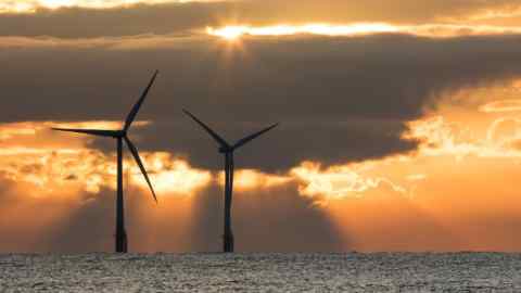 Offshore wind turbines silhouetted against a dramatic sunset