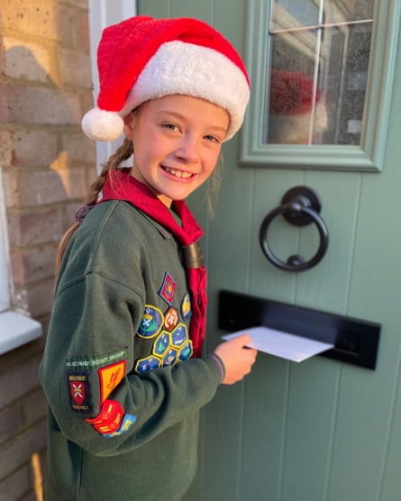 Smiling girl in Scout uniform and Christmas hat posting letter through letterbox