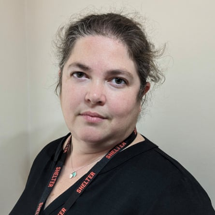 Ruth Camp, hair pulled back and wearing a lanyard ribbon stamped “Shelter”, looks at the camera barely smiling