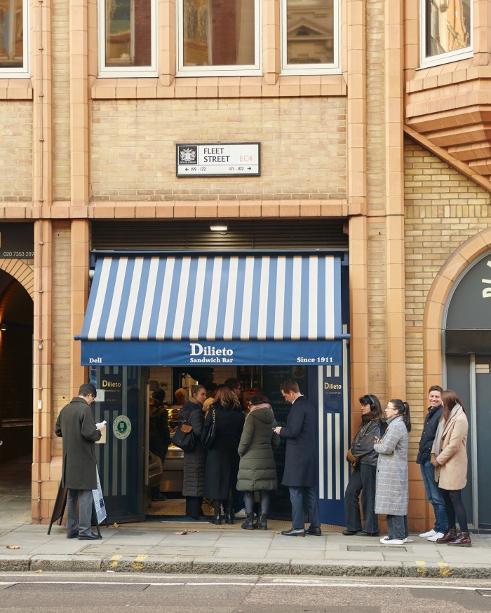 A queue of people in the street outside Dilieto. On the wall above its blue and white striped awning is a sign that says ‘Fleet Street’