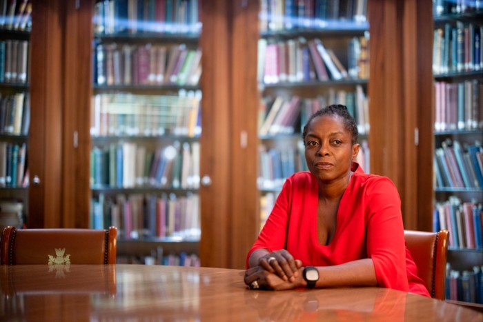 A middle-aged woman in a red blouse sits at a table in a library