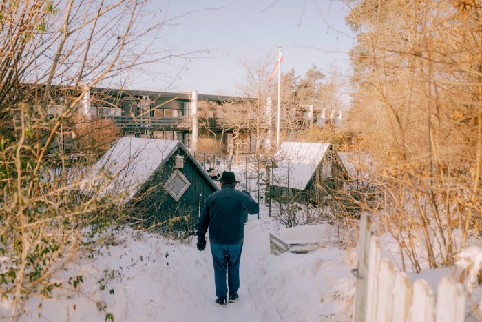 Morten walks down a snowy path towards an allotment with green wooden sheds