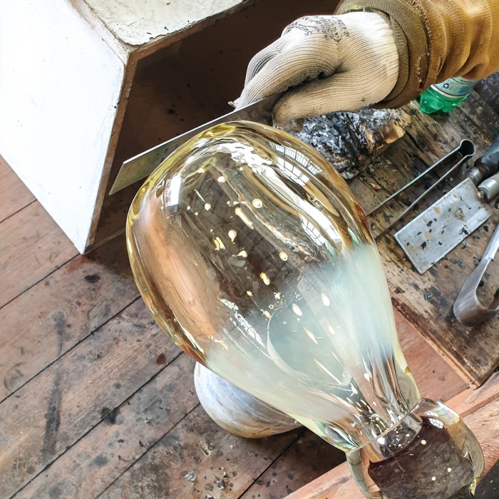 Gloved hands work on the vessel at a glassworks