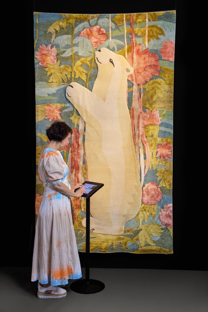 A woman examines an interactive screen next to a tapestry of a polar bear among flowers