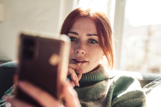 Woman with red hair looking on screen of her mobile phone.