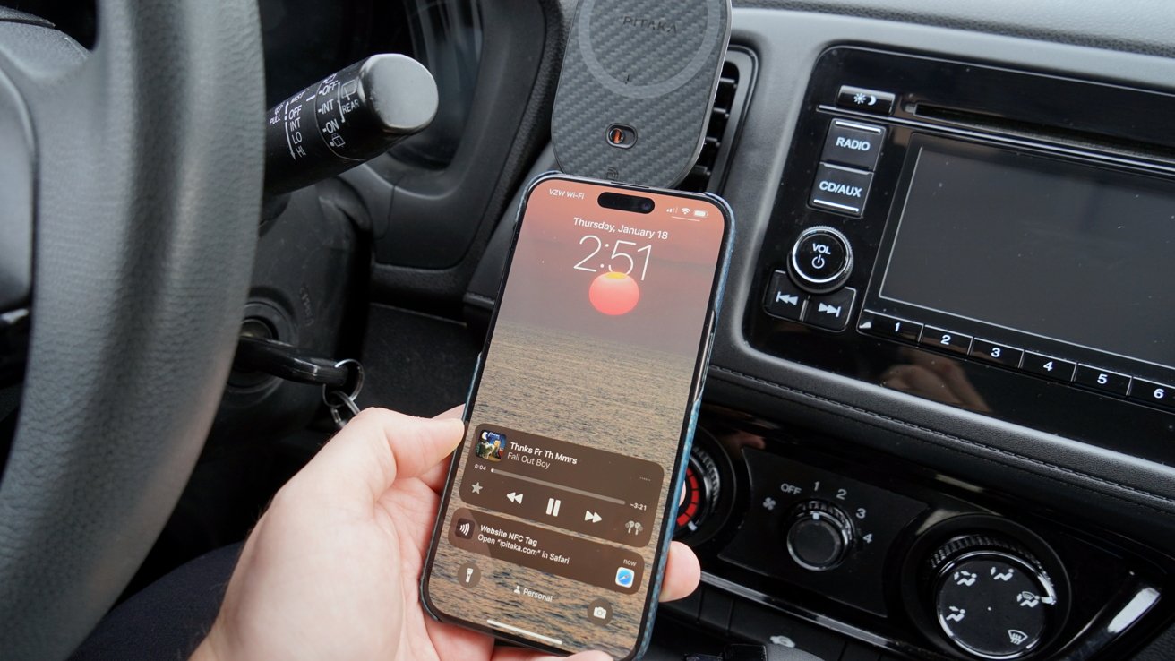 An iPhone with a sunset as its background in a blue case taps the Pitaka charger near an NFC symbol. An automation to play music is run and shown on the display.