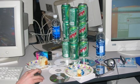 A desk with computers, CD-Rs, a digital camera, headphones and a keyboard with someone's hand on the mouse