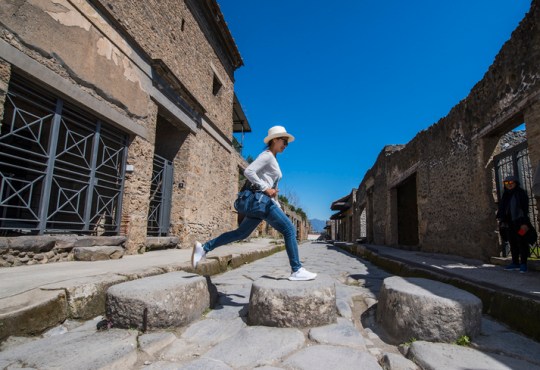 Female tourist jumping on stones in Pompeii