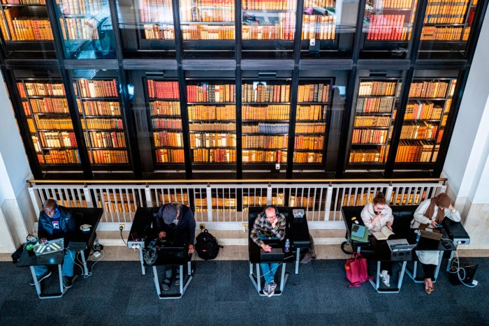 Members of the public at the British Library,  with the books of the kings collection behind them. 