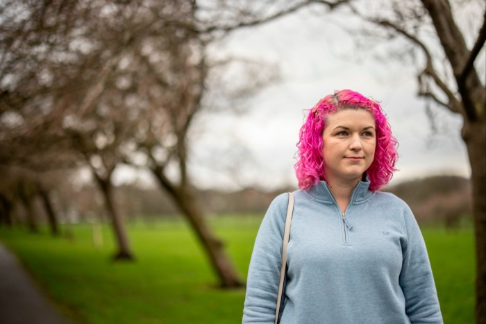 A young woman with pink hair stands in a park