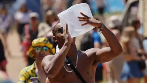 PA A man walking through the festival site on a hot day is seen drinking from a large plastic water container. 