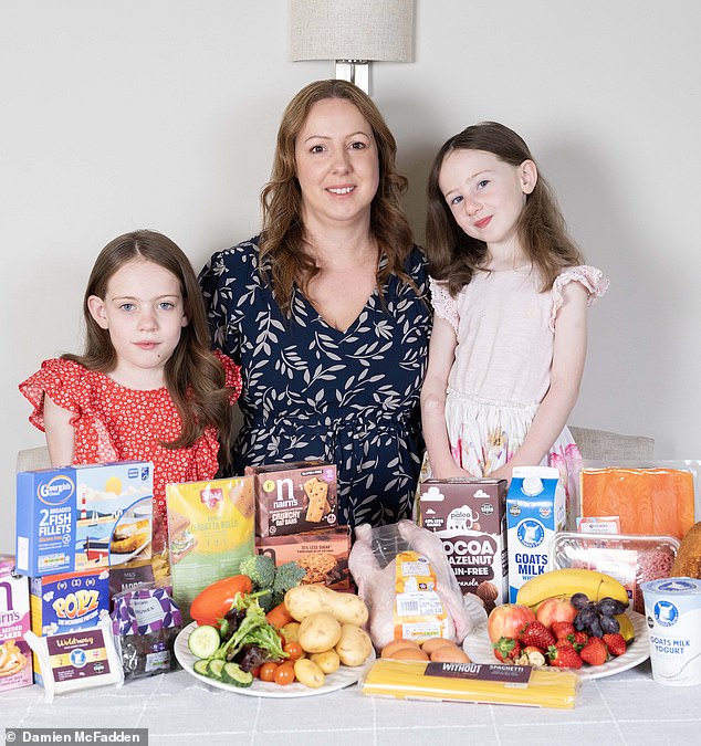Kate Rawlings with her daughters Isobel, eight, and Sophie, four. The table has a collection of the foods that make up Isobel's new diet, including goat's milk and gluten-free products