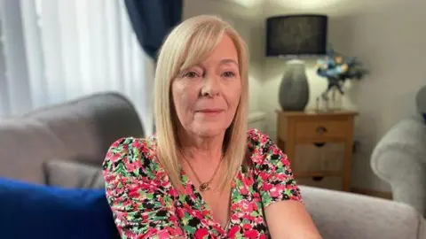 BBC Sylvia Vickery, a woman with blonde hair looking directly to camera wearing a pink and green floral dress