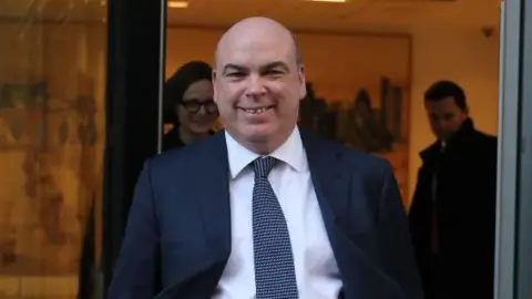 Getty Images Mick Lynch smiles wearing a suit as he leaves a building