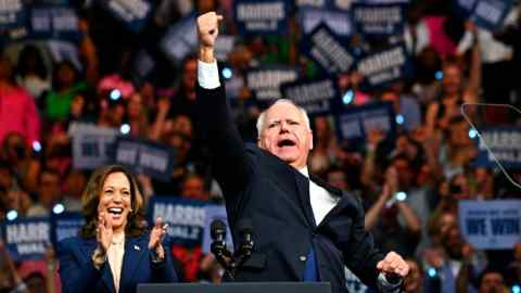 A man standing at a podium punches the air while a woman standing behind him claps and a crowd cheers