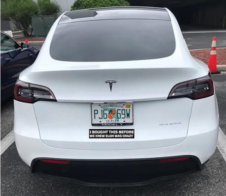 A bumper sticker on a white Tesla car says ‘I bought this before we knew Elon was crazy.’