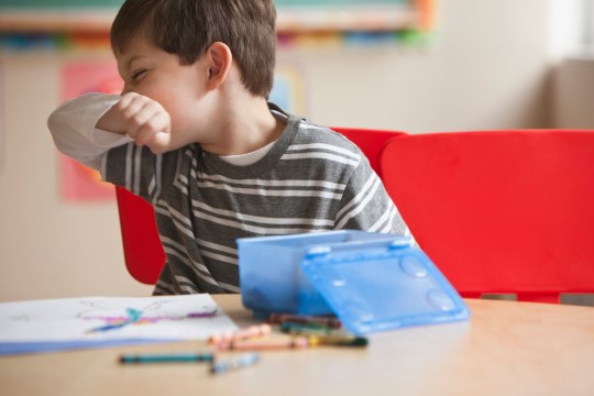 A boy sneezing in the back of his hand. 