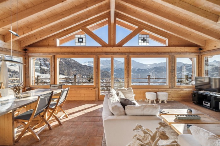 Timber A-framed room with full picture windows looks out on snowy mountains