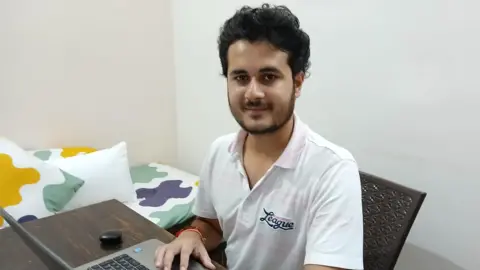 Anurag Garg Anurag Garg sitting at his computer wearing a white shirt.