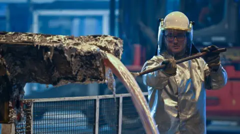 Getty Images Wearing a protective silver suit a worker collects molten aluminium samples at a aluminium recycling and production plant, in eastern France. 