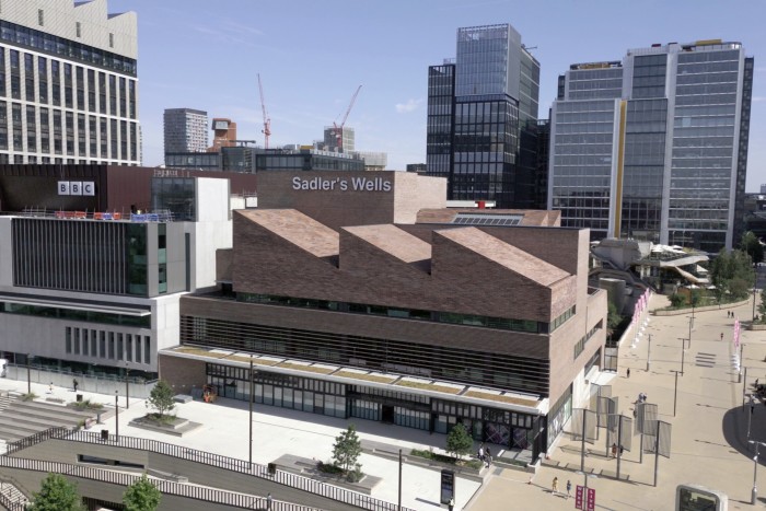 A new building bearing the words ‘Sadler’s Wells’ on one wall. It is surrounded by other, taller buildings, and to one side is a pedestrianised area.